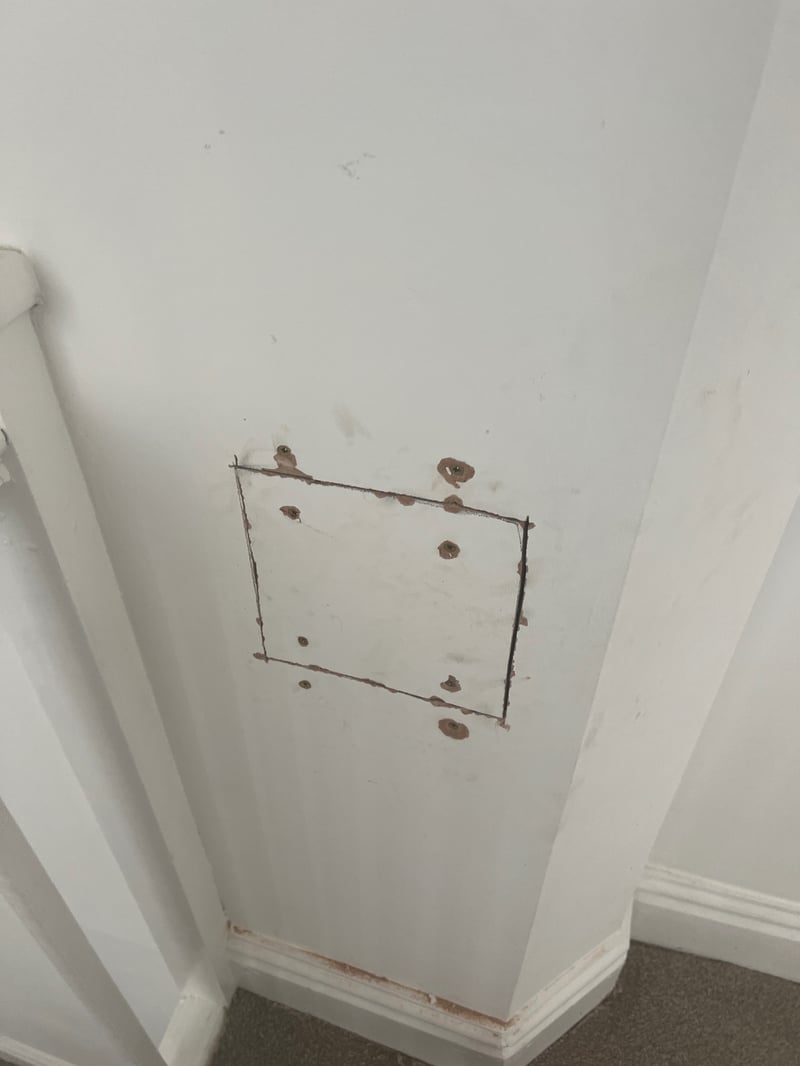 Wall with a filled cut-out patch and old fixing holes before making good