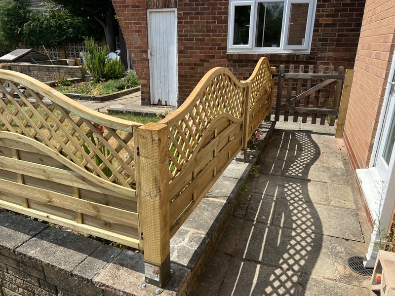 Close view of completed timber fence panels and posts fixed to the wall on metal post supports