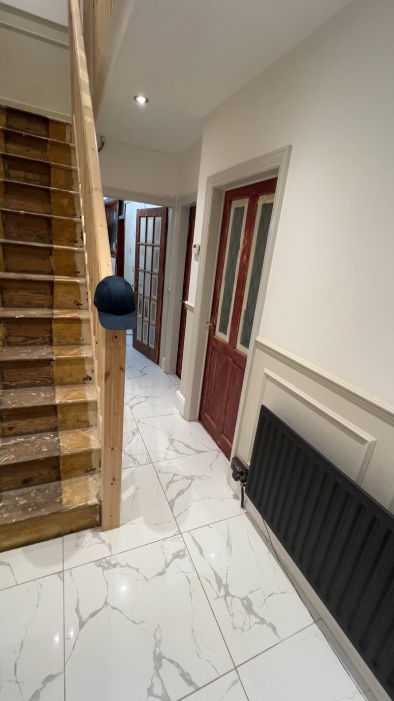 Completed hallway showing the bottom of the stairs, marble-effect floor tiles and new radiator