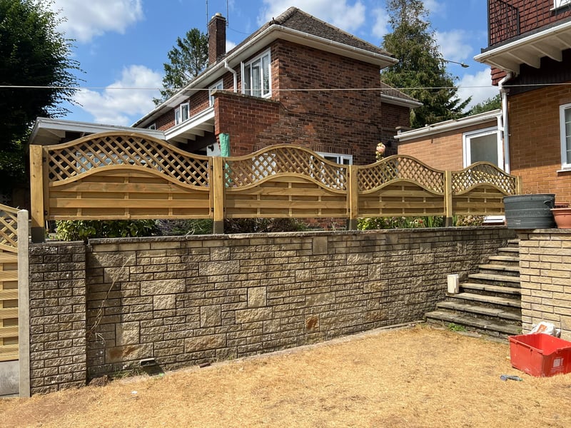 Completed run of wave-top lattice timber fence panels fitted along a raised garden wall