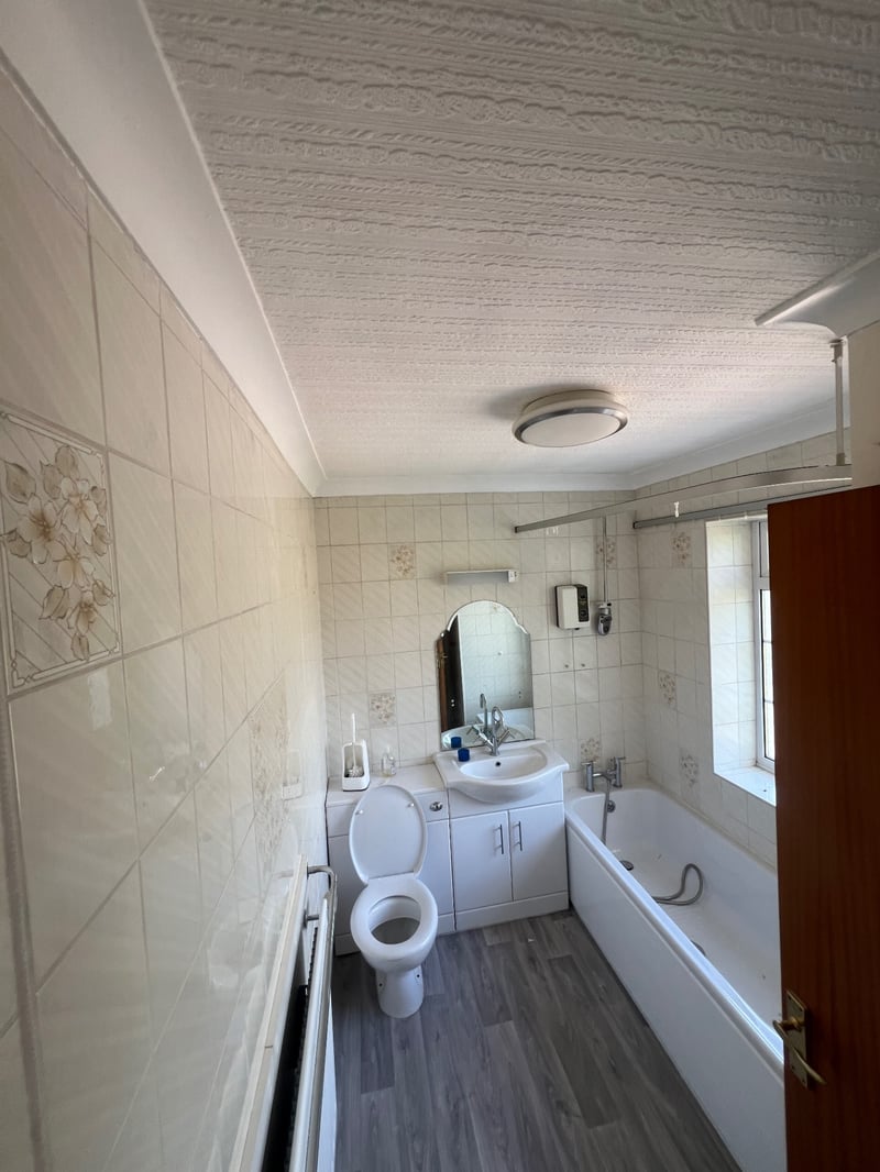 Dated bathroom with patterned cream wall tiles, white bath and vanity unit before renovation